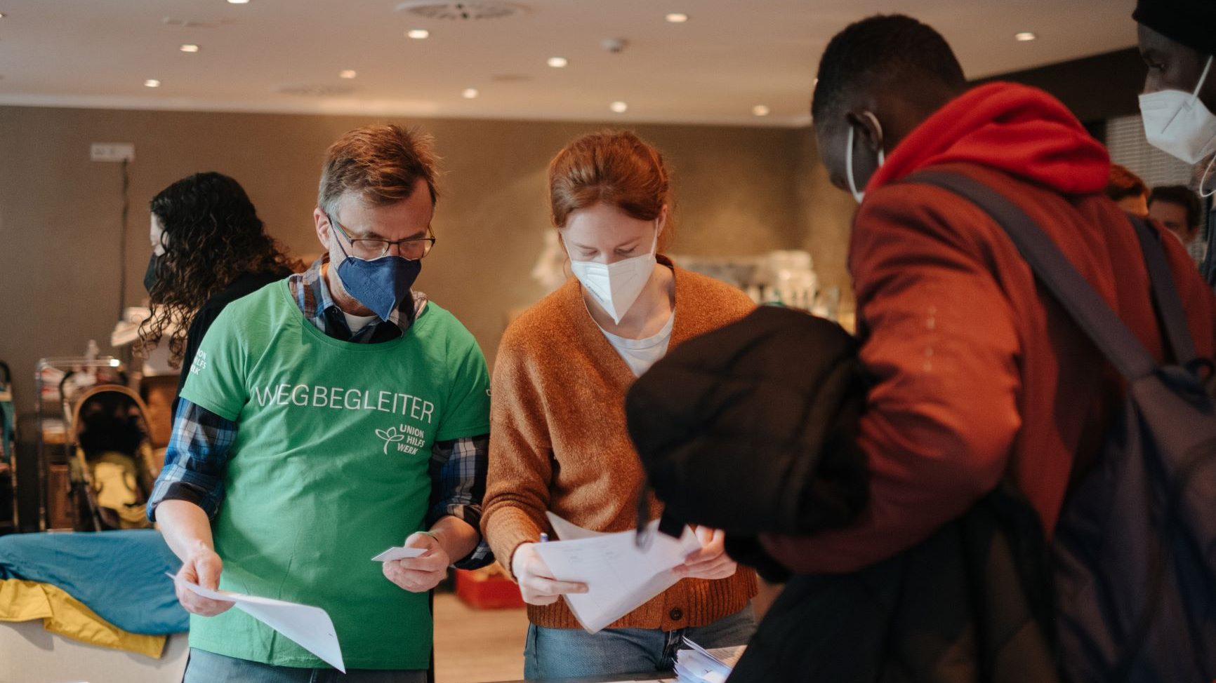 drei Personen mit Maske schauen auf Unterkage stehend