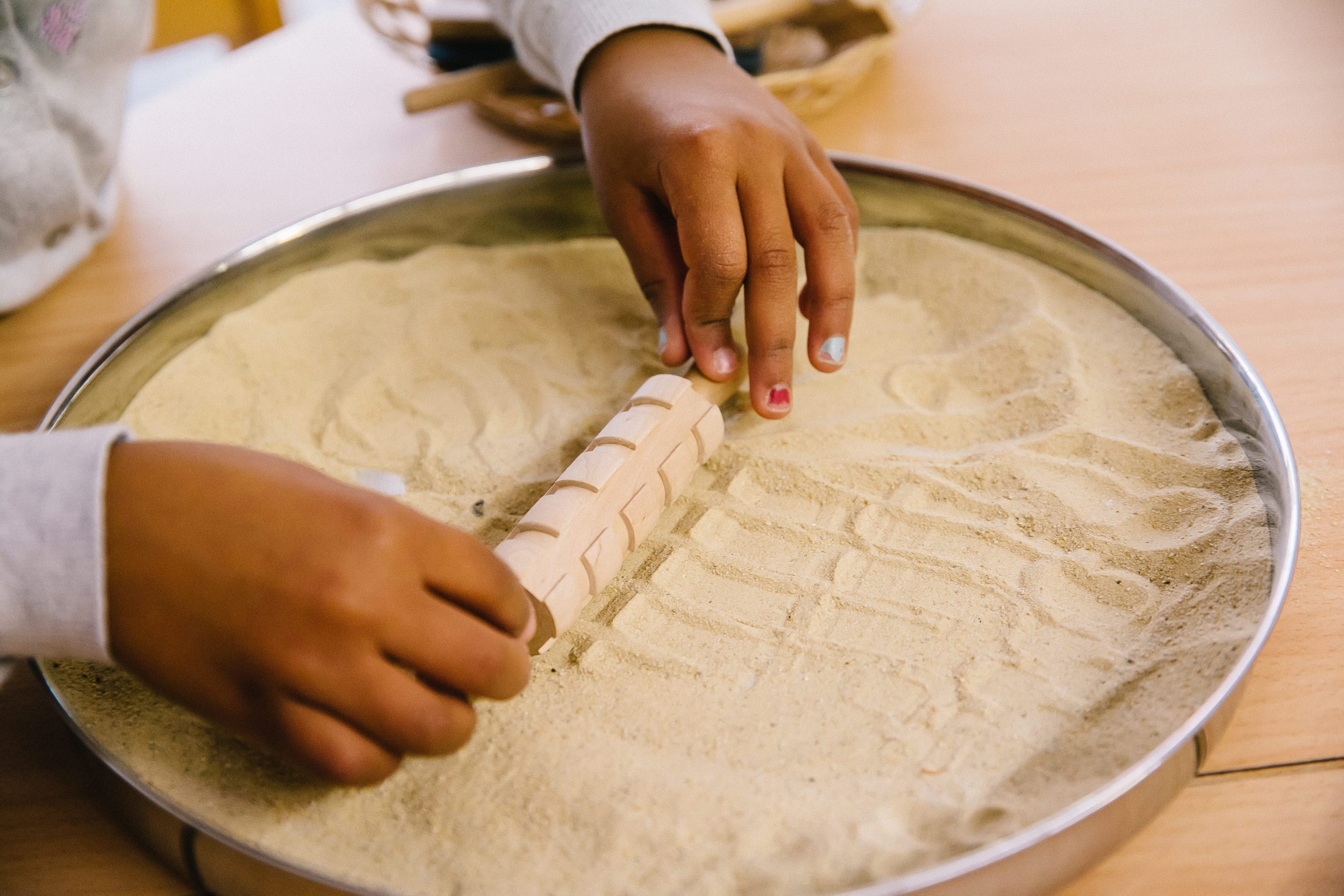 Kinderhände mit Teigrolle auf Sand