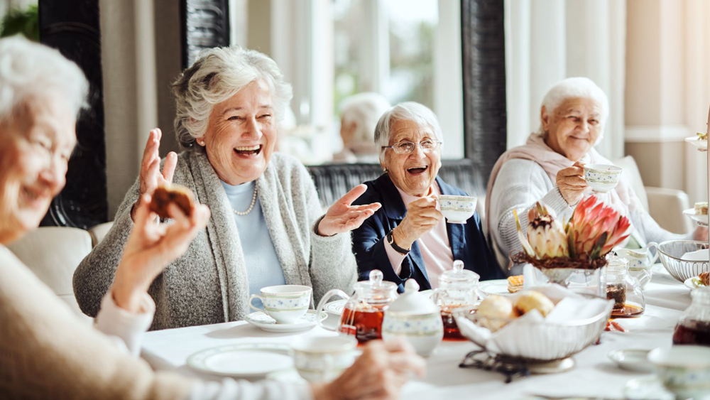 vier Seniorinnen am Teetisch lachend mit Teetassen