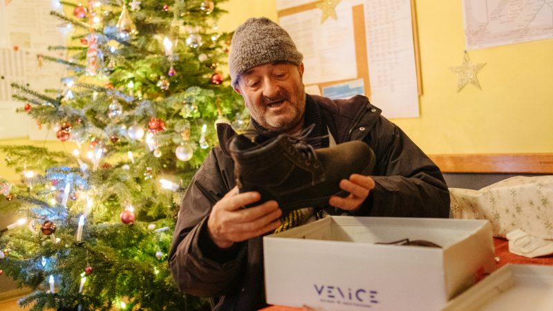 Mann holt Schuhe aus Karton hinter ihm Weihnachtsbaum