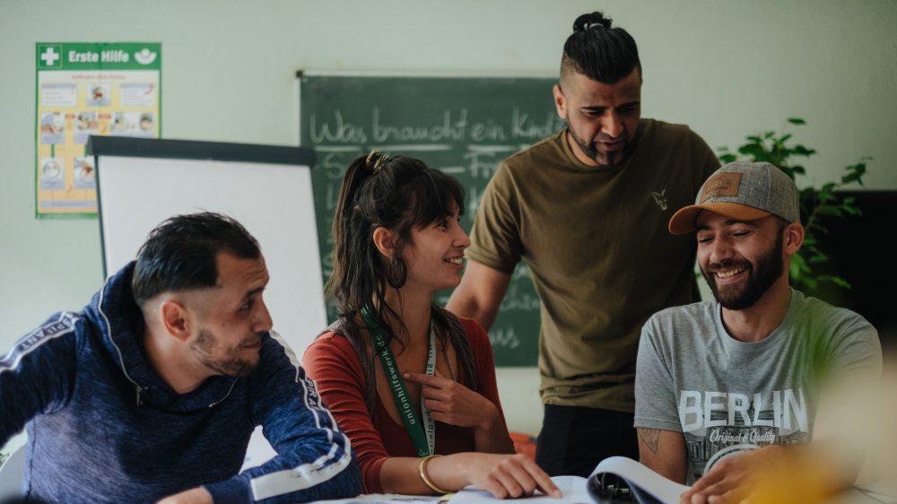 drei Männer eine Frau lachend im Klassenzimmer