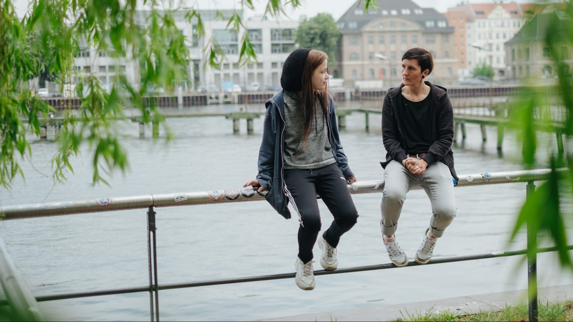 zwei Personen sitzen auf Planke vor Fluss