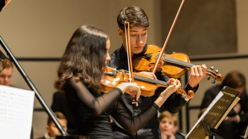 Ein junger Mann und eine junge Frau spielen Geige bei einem Konzert.